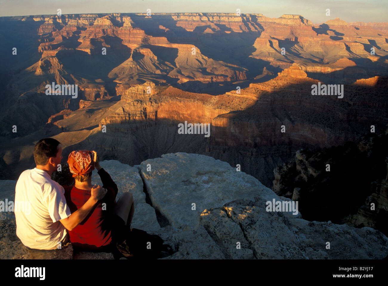 A man and a woman sit together at the edge of the Grand Canyon at near ...