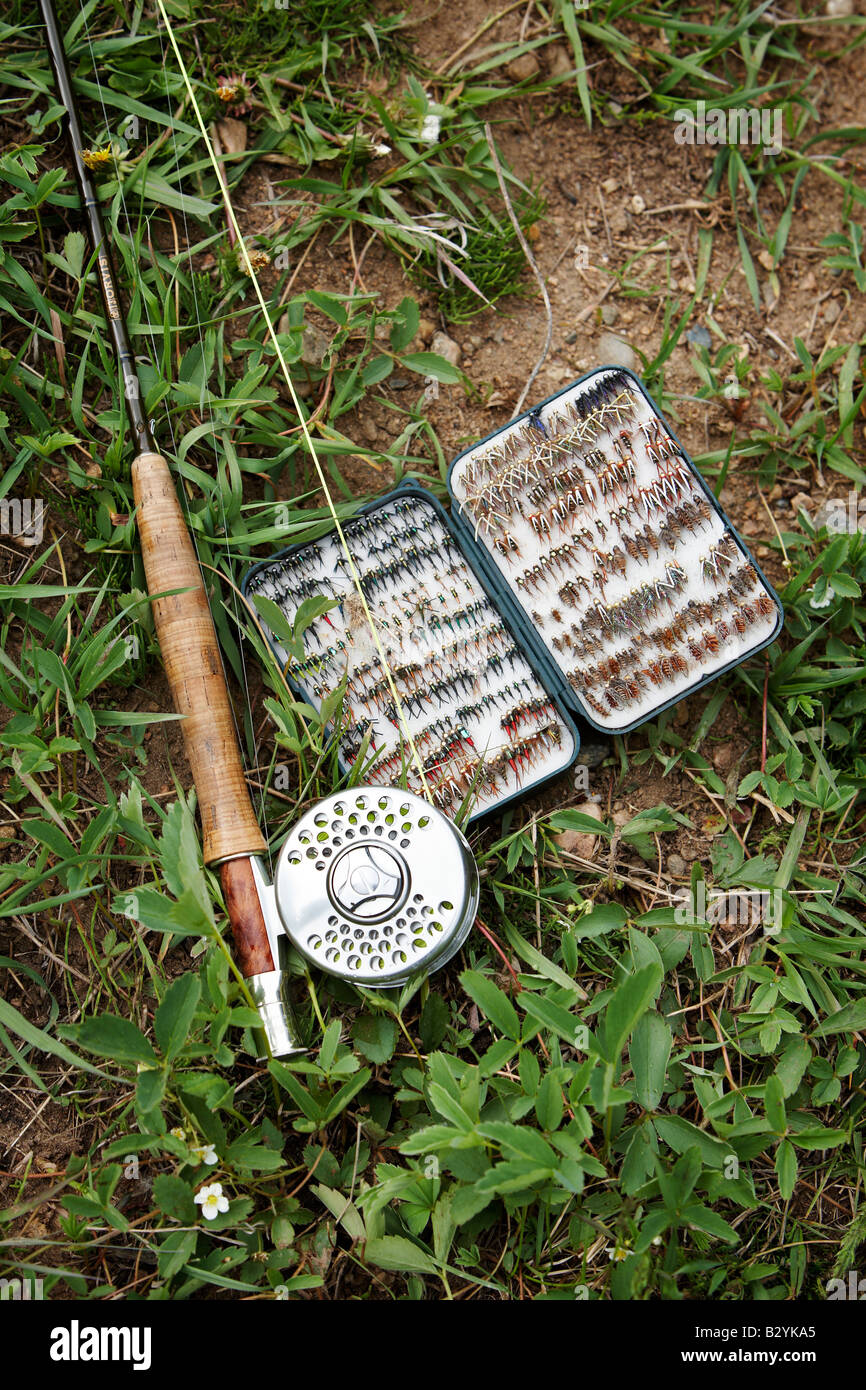 A fly rod with reel and tackle box sit on a grassy river bank Stock