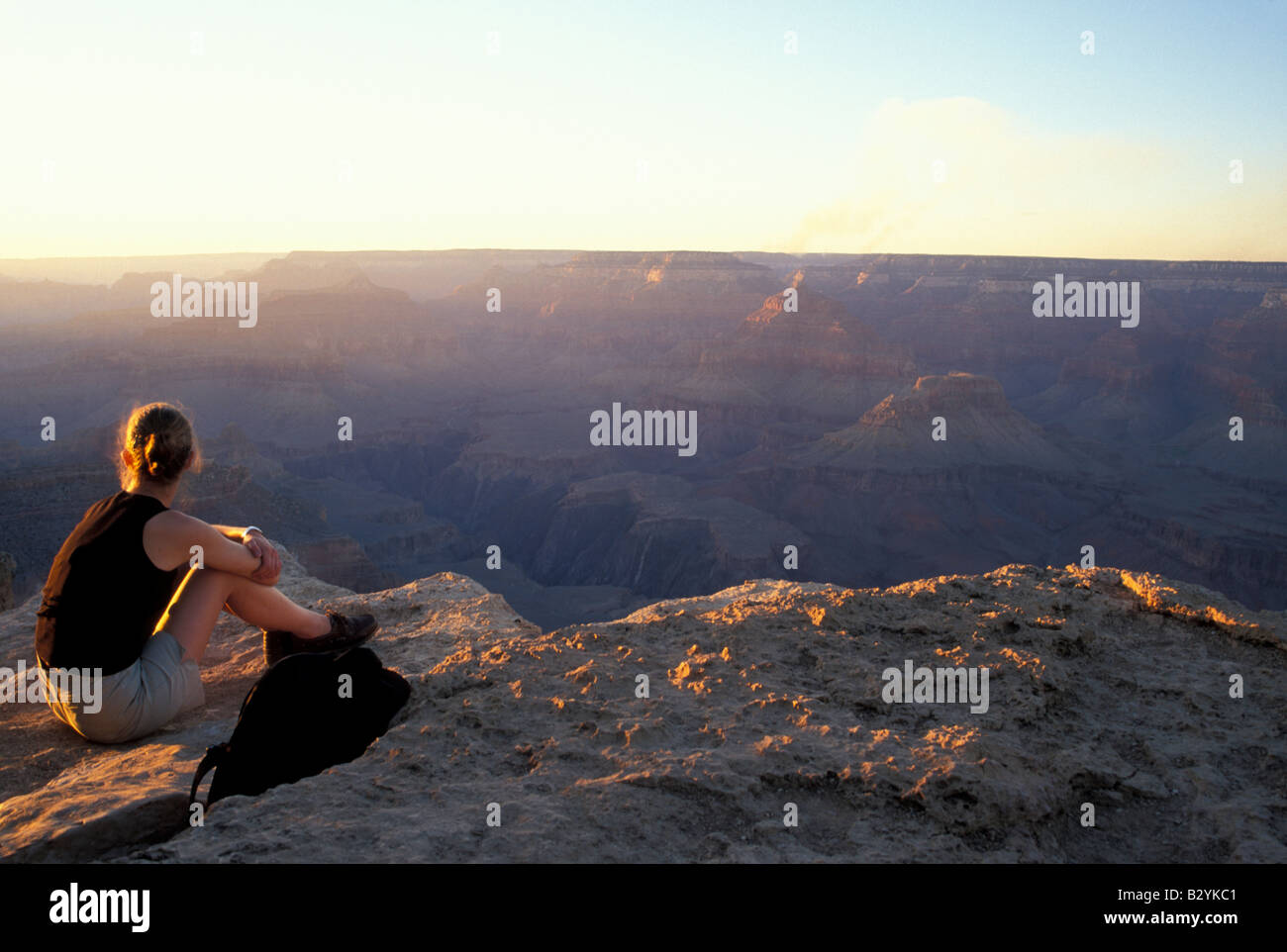 A woman sits at the edge of the Grand Canyon at sunset in Grand Canyon ...