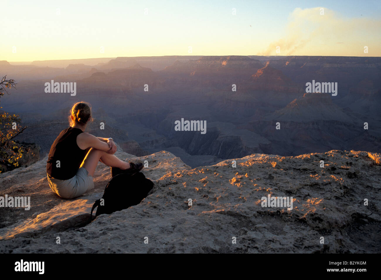 A woman sits at the edge of the Grand Canyon at sunset in Grand Canyon ...