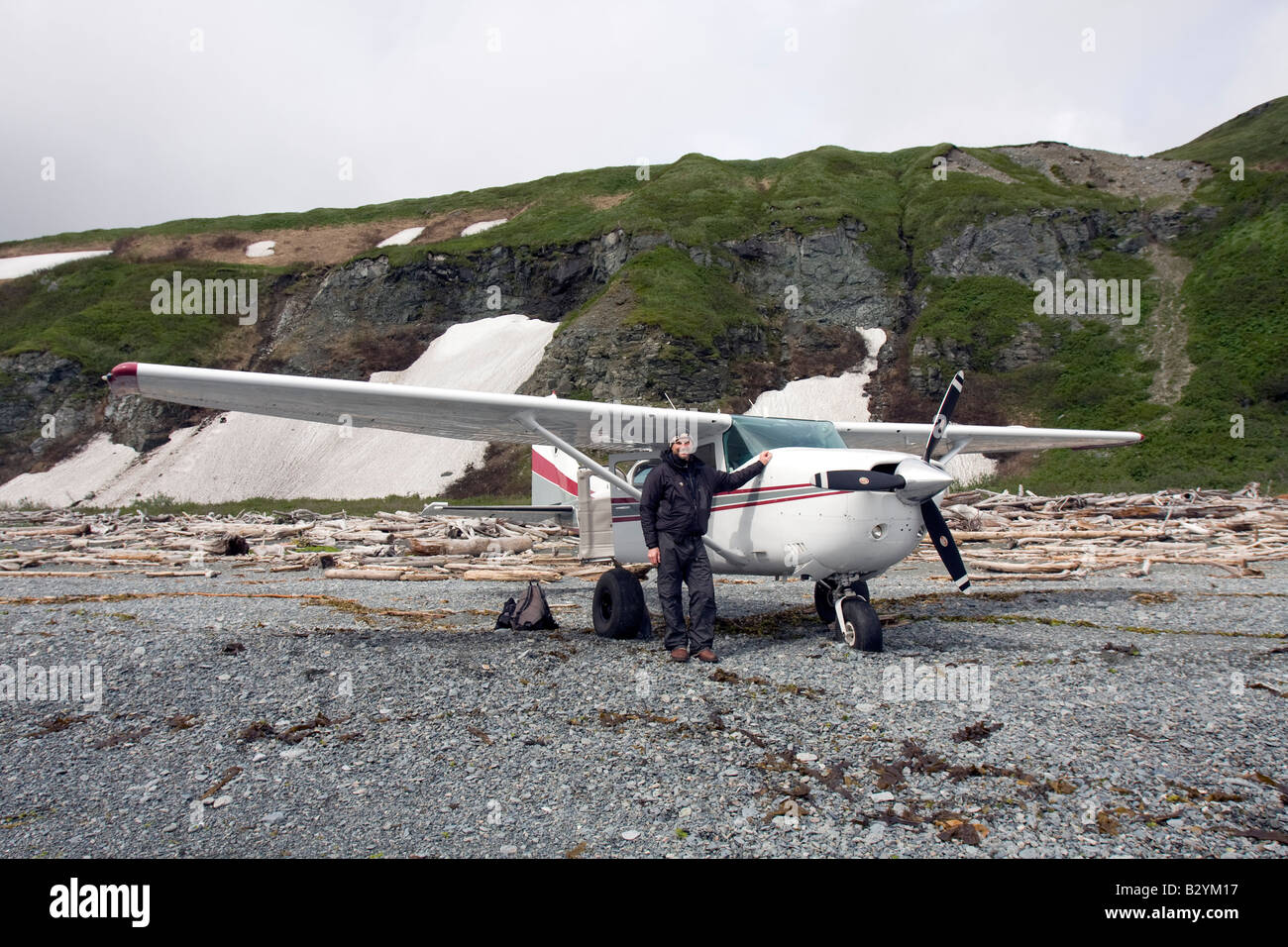 K-Bay Air air plane (Cessna 206) and pilot standing on a beach filled with driftwood in the Katmai National Park and Preserve, Alaska, US Stock Photo