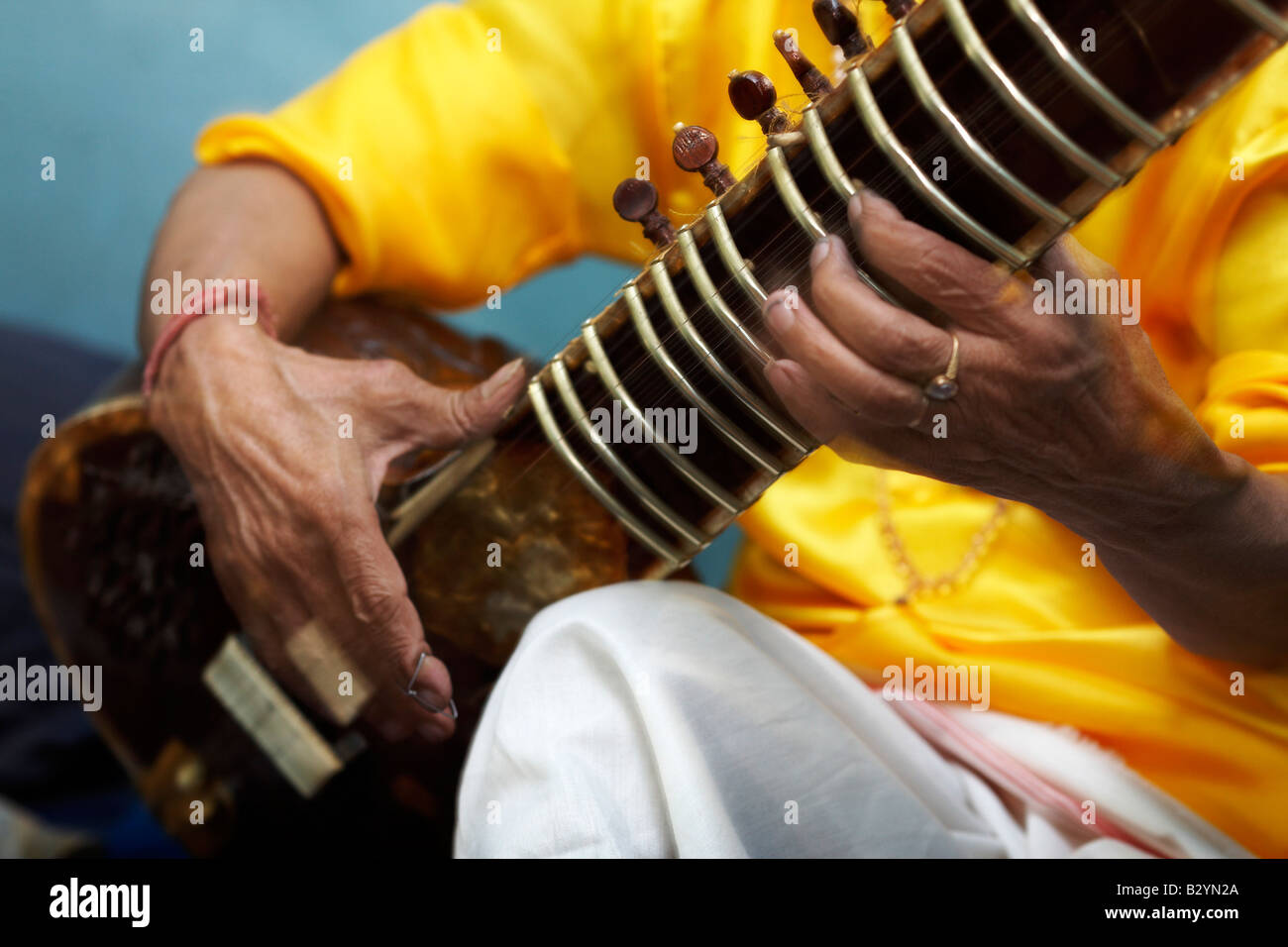 A closeup of the hands and instrument of a colorful Indian sitar player as he sits and plays