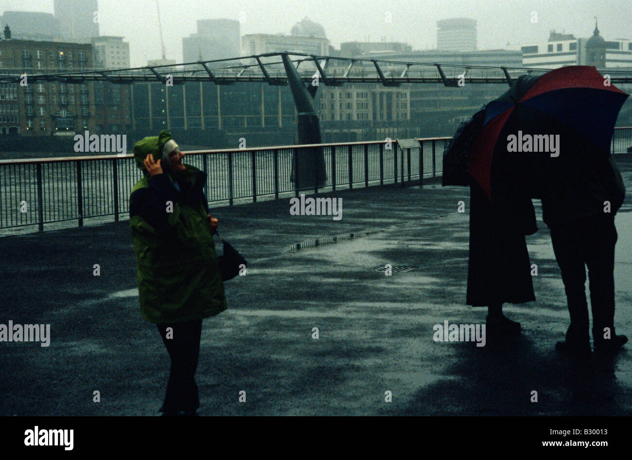 Pedestrians taking cover from rain along the riverfront in London. Stock Photo