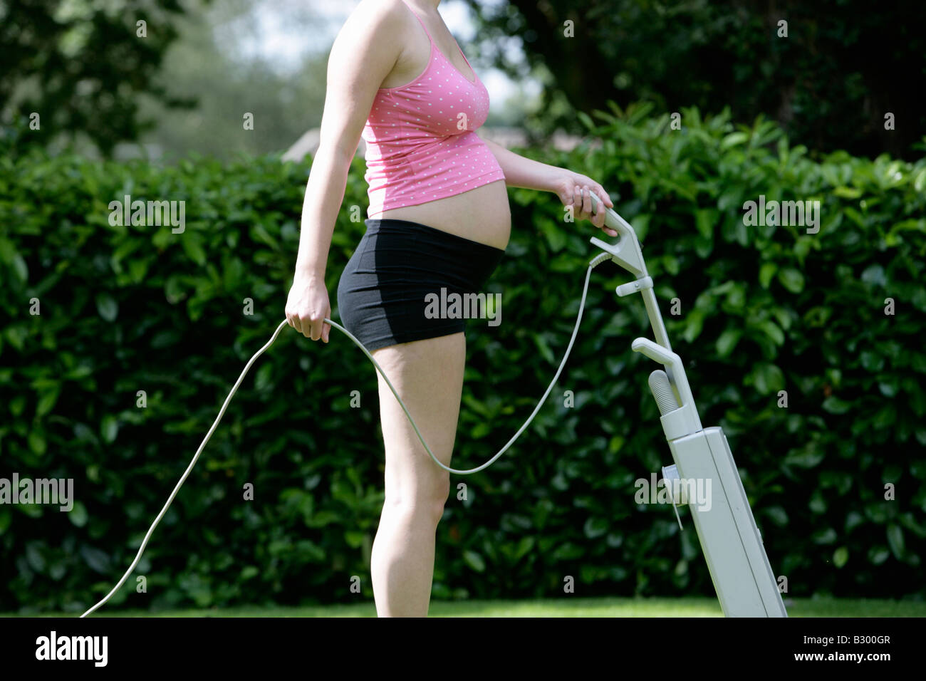 Pregnant Woman Mowing Lawn with Vaccuum Cleaner Stock Photo