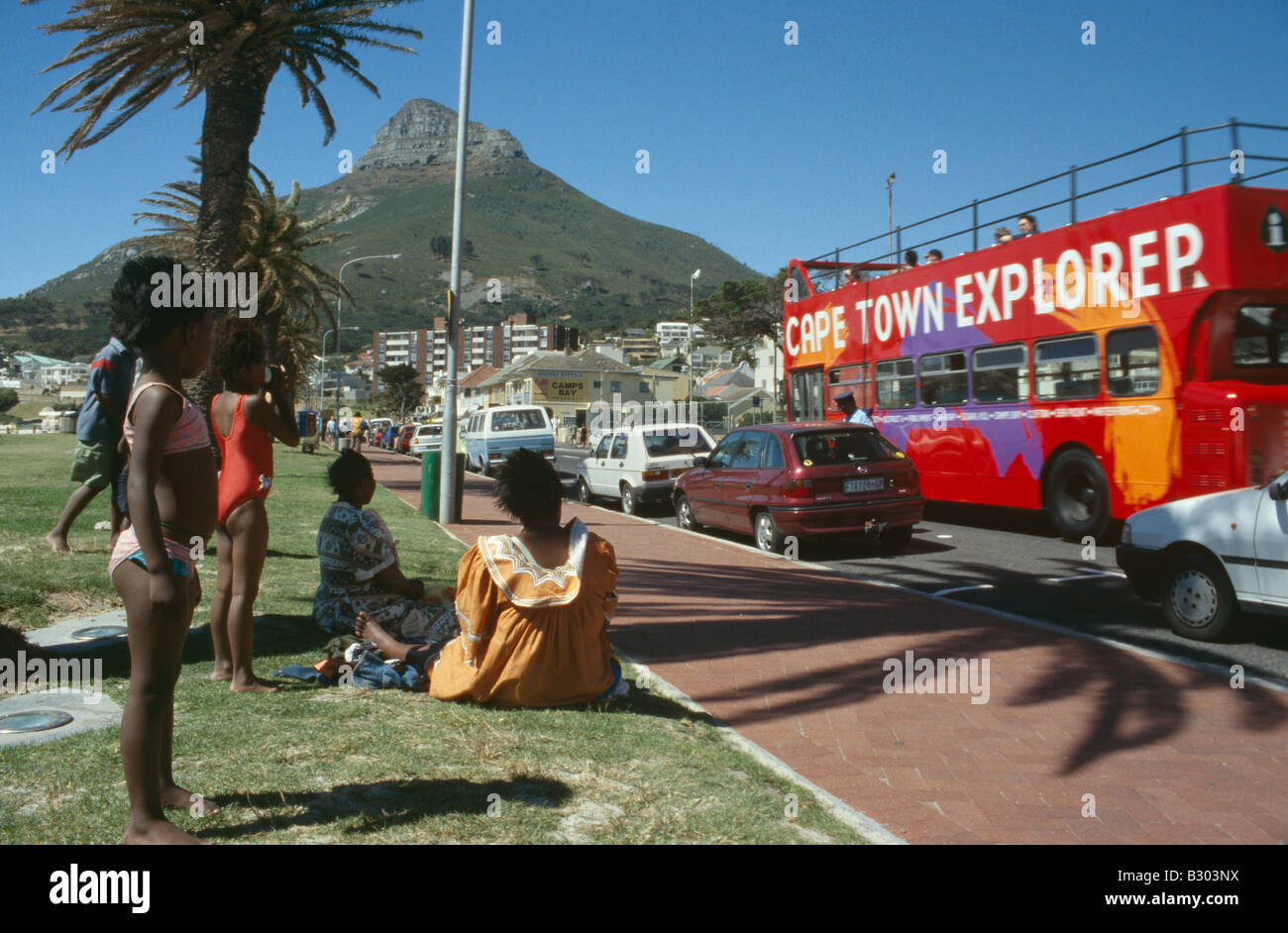 City scene with people sitting by road side watching traffic pass. Cape