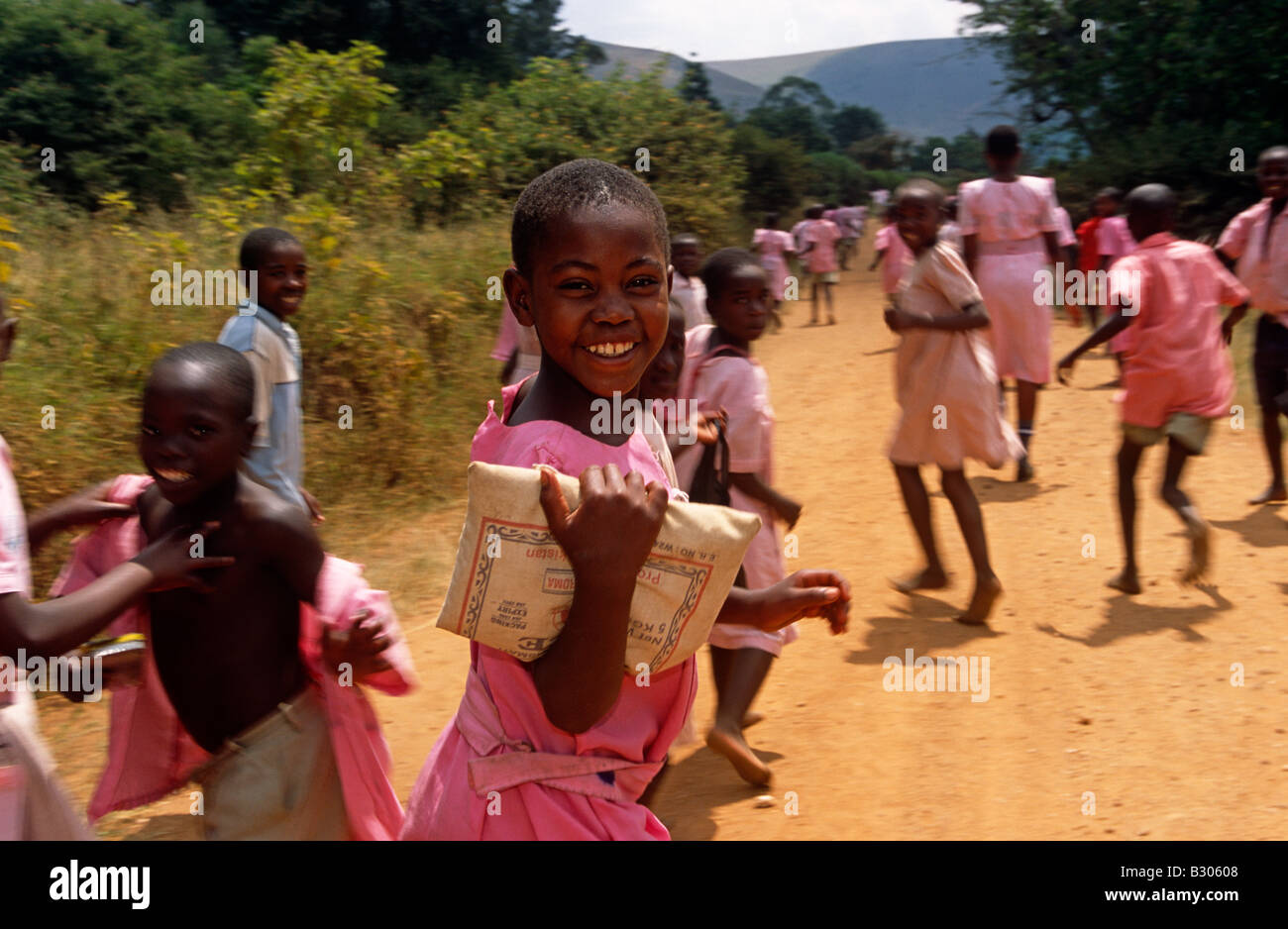 Crowd of schoolchildren running along dirt track in pink uniforms, Uganda, Africa Stock Photo