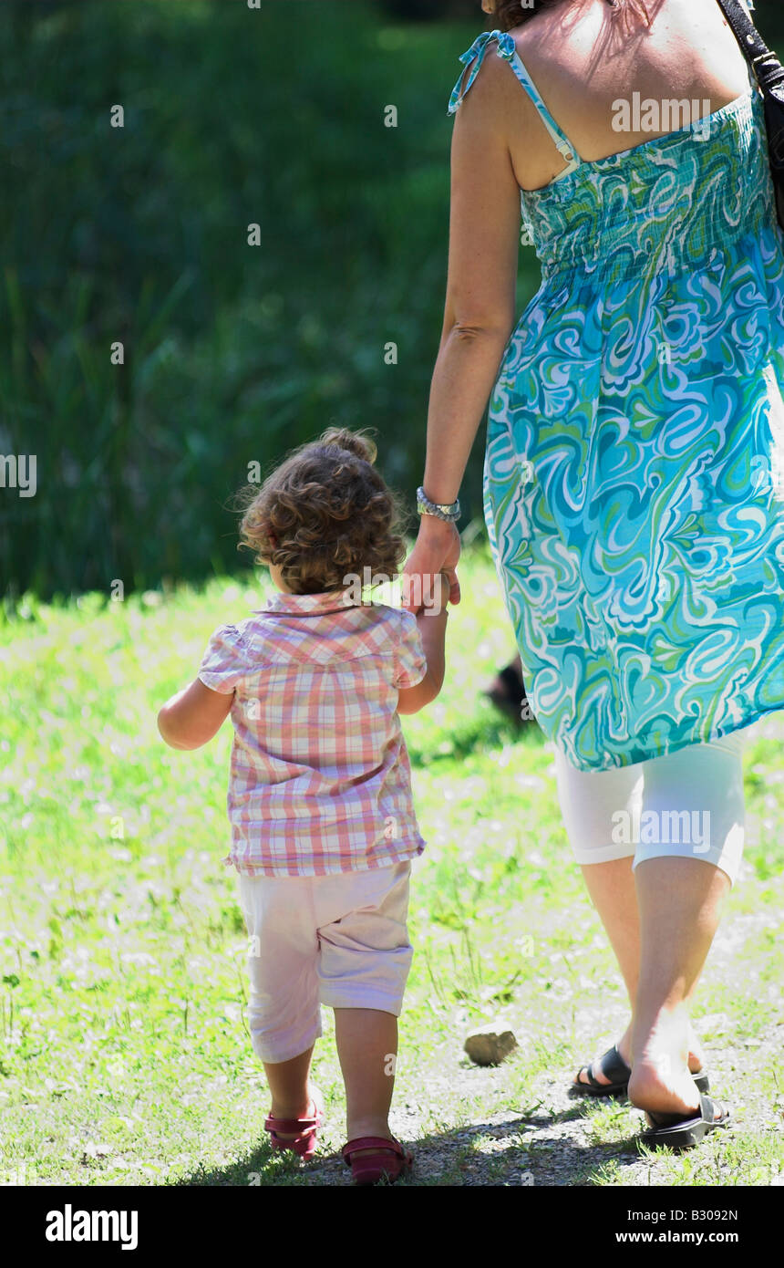 Mother and daughter 2 3 walking on meadow hand in hand rear view Stock Photo
