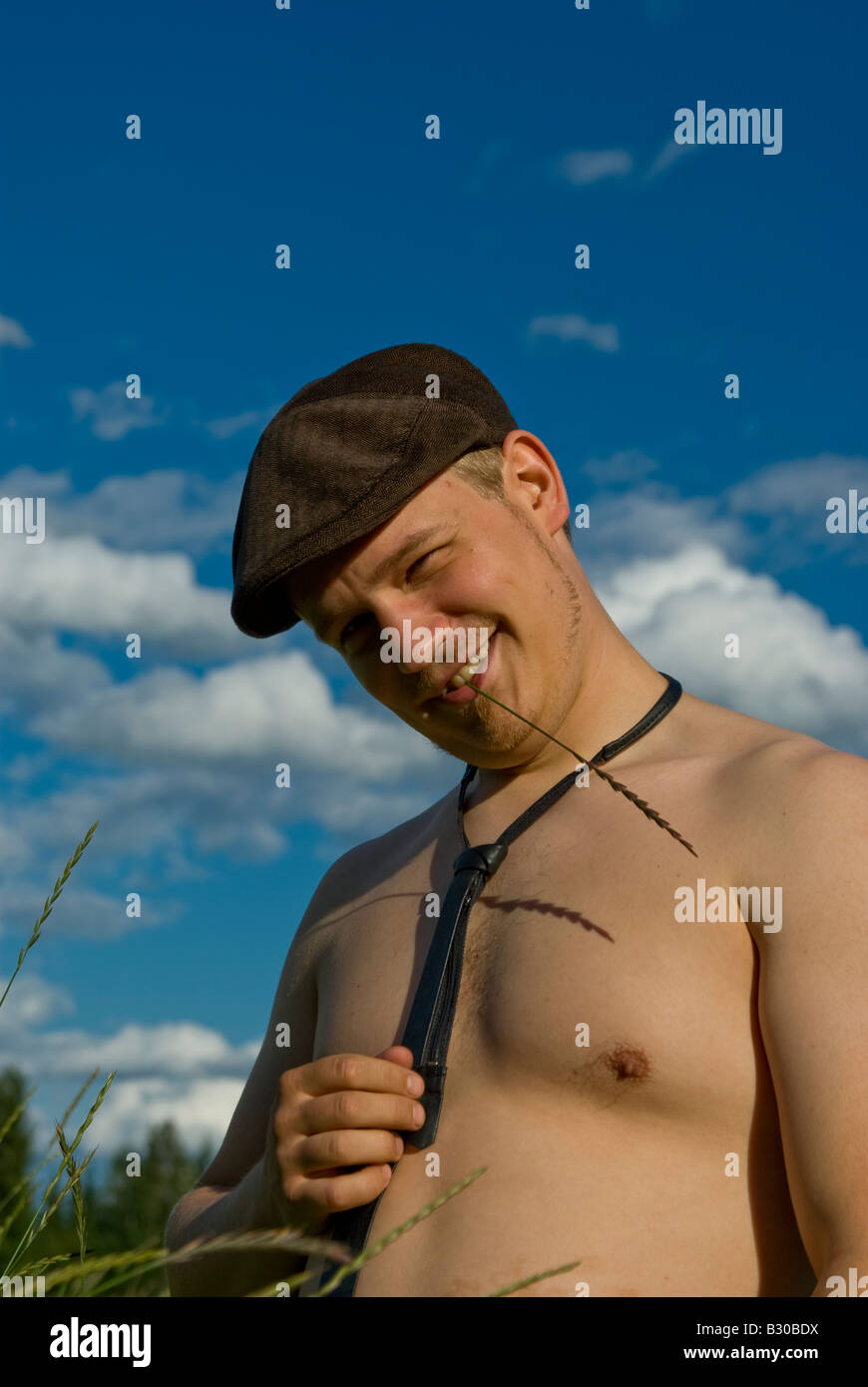 A guy on a field on a sunny day with a straw in his mouth Stock Photo