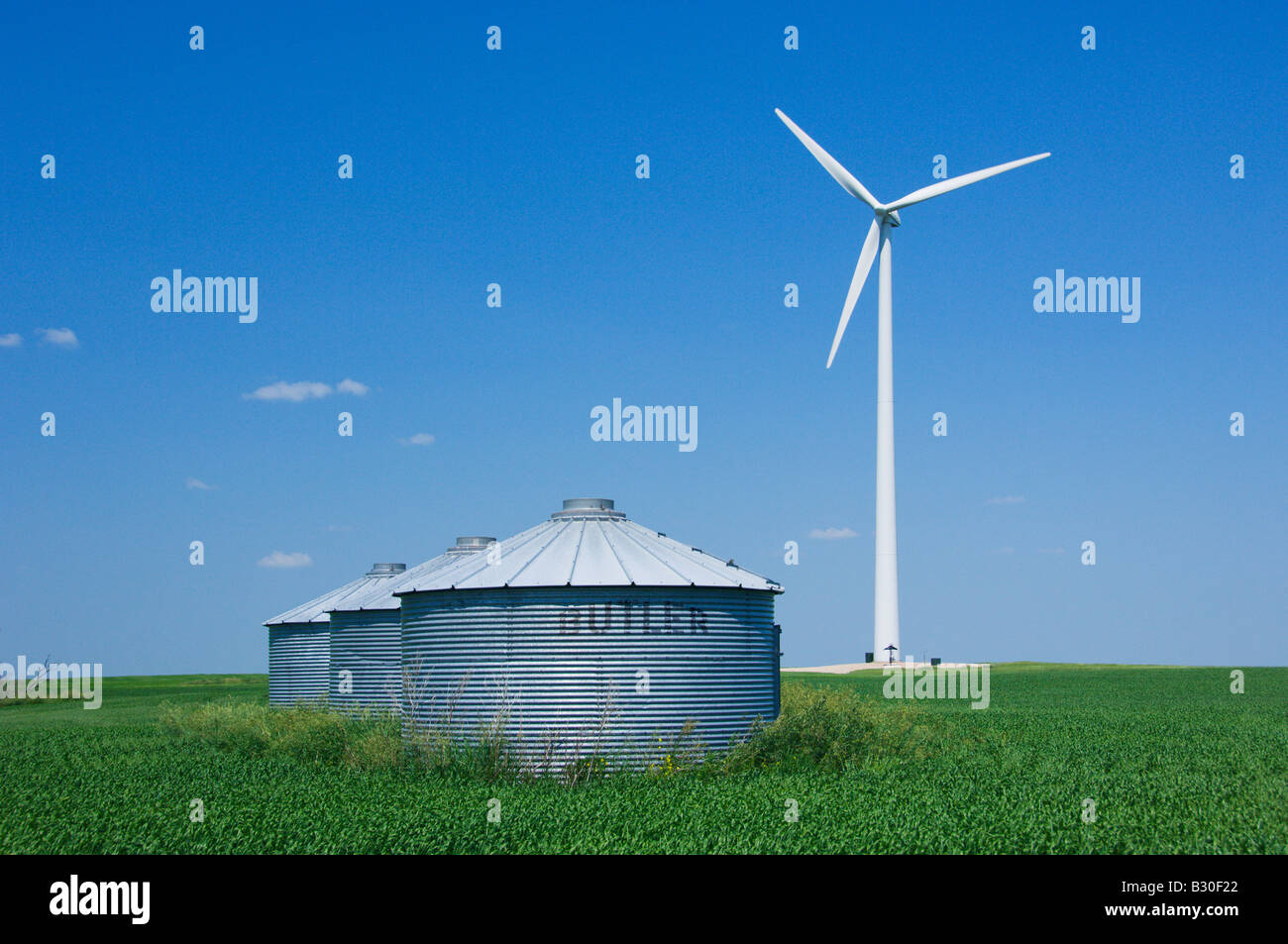 A windmill generating electricity in a field of grain with storage bins
