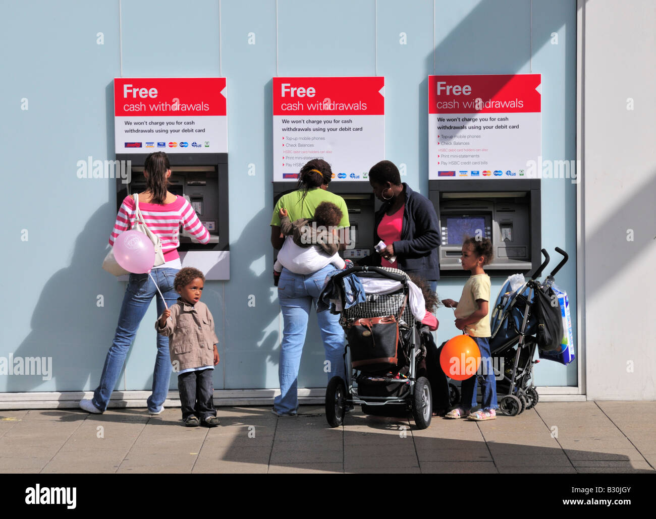 A family with prams, children and a baby, holding balloons, with a single female, using HSBC bank cash machines in Kingston, UK Stock Photo