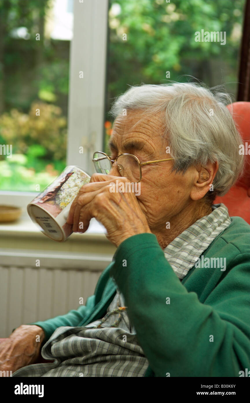 Elderly woman of 92 years sitting drinking tea from a mug in living room Stock Photo