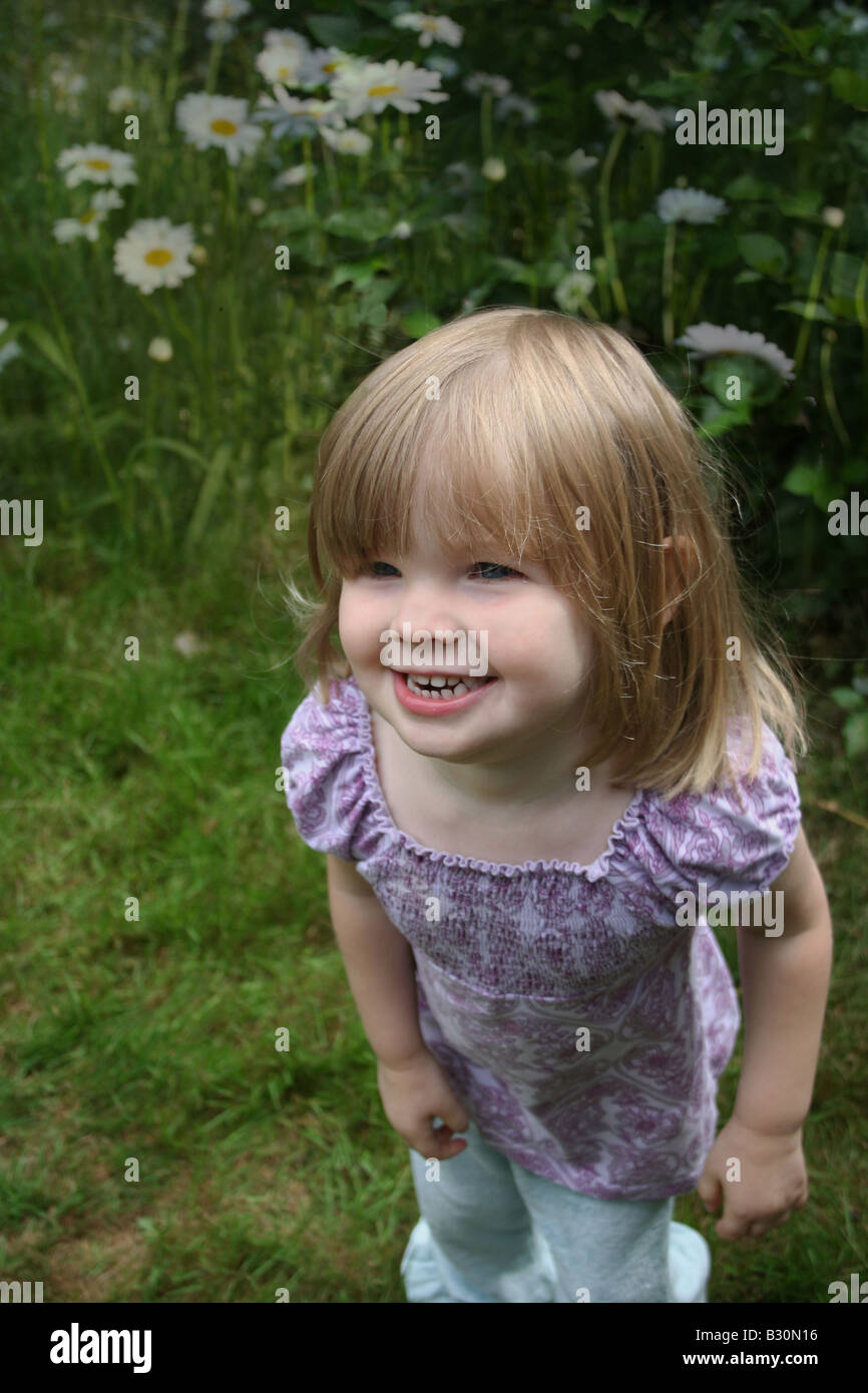 Happy cute pretty young girl laughing outside in spring or summer on green grass with daisy's behind her Stock Photo