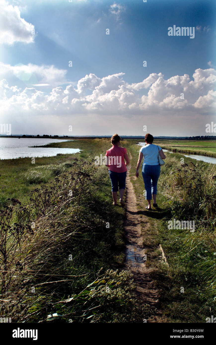 two middle aged women walking together on path over marshes at Aldeburgh Suffolk England Stock Photo