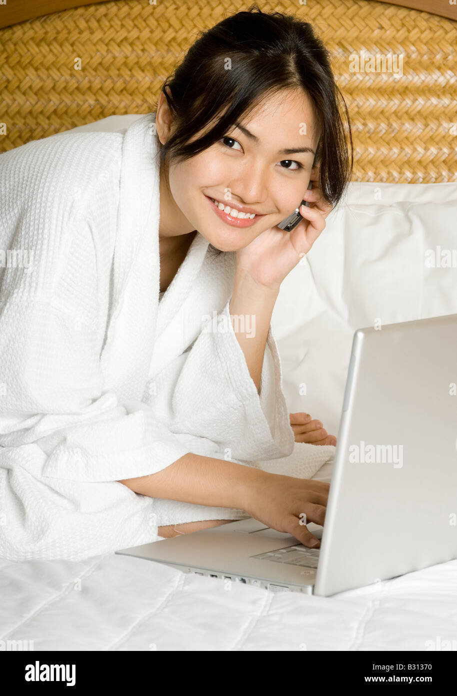 A pretty young asian woman on a bed with laptop and phone Stock Photo ...