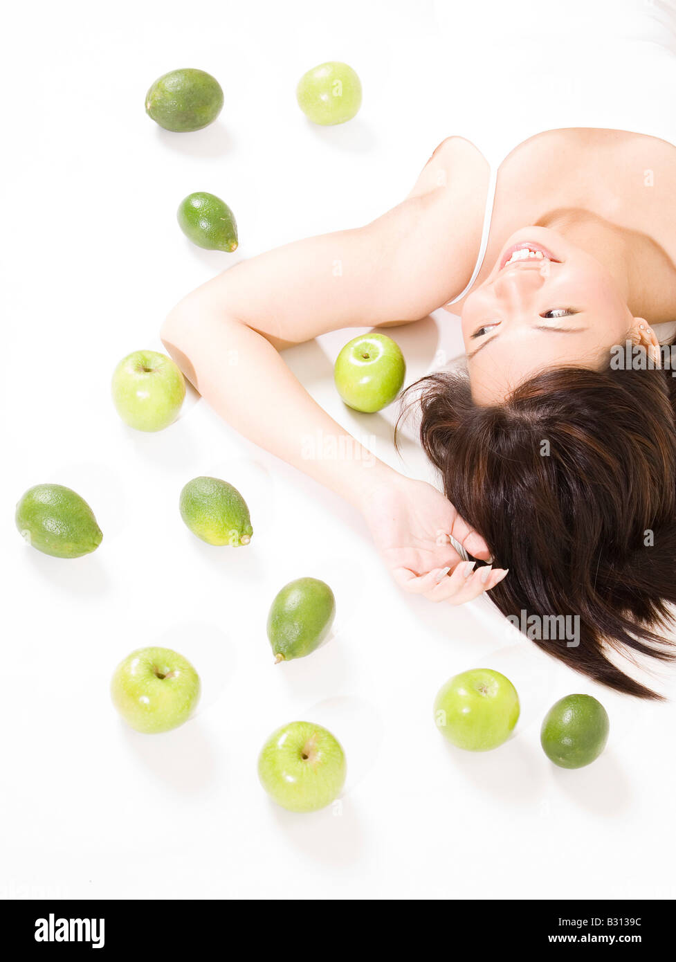 A pretty young asian woman on a white background with green colored fruits Stock Photo