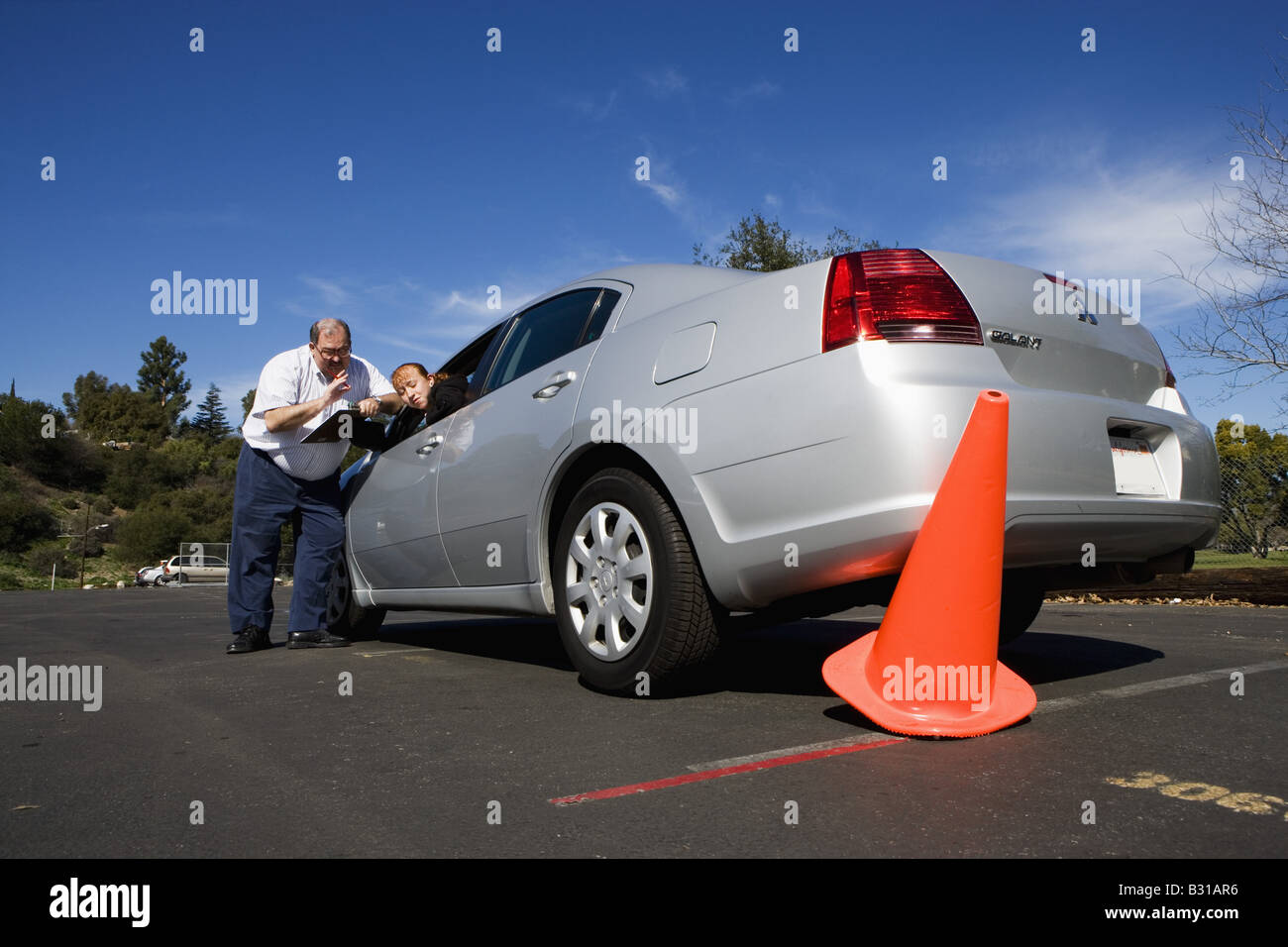 Driving instructor discusses knocked over orange cone with teen Stock Photo