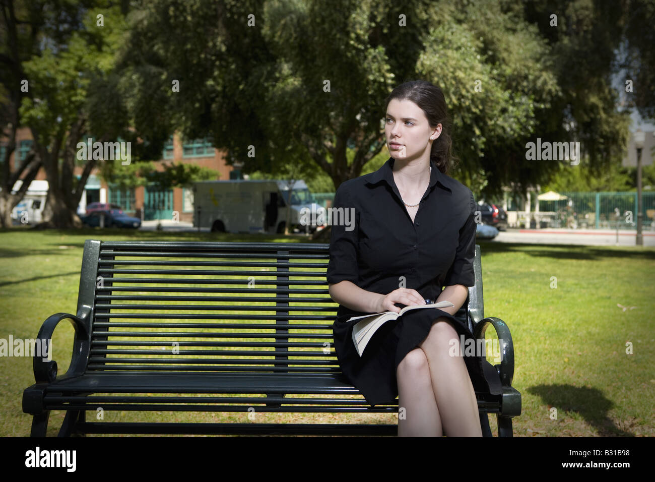 Young woman sitting on park bench with book Stock Photo - Alamy