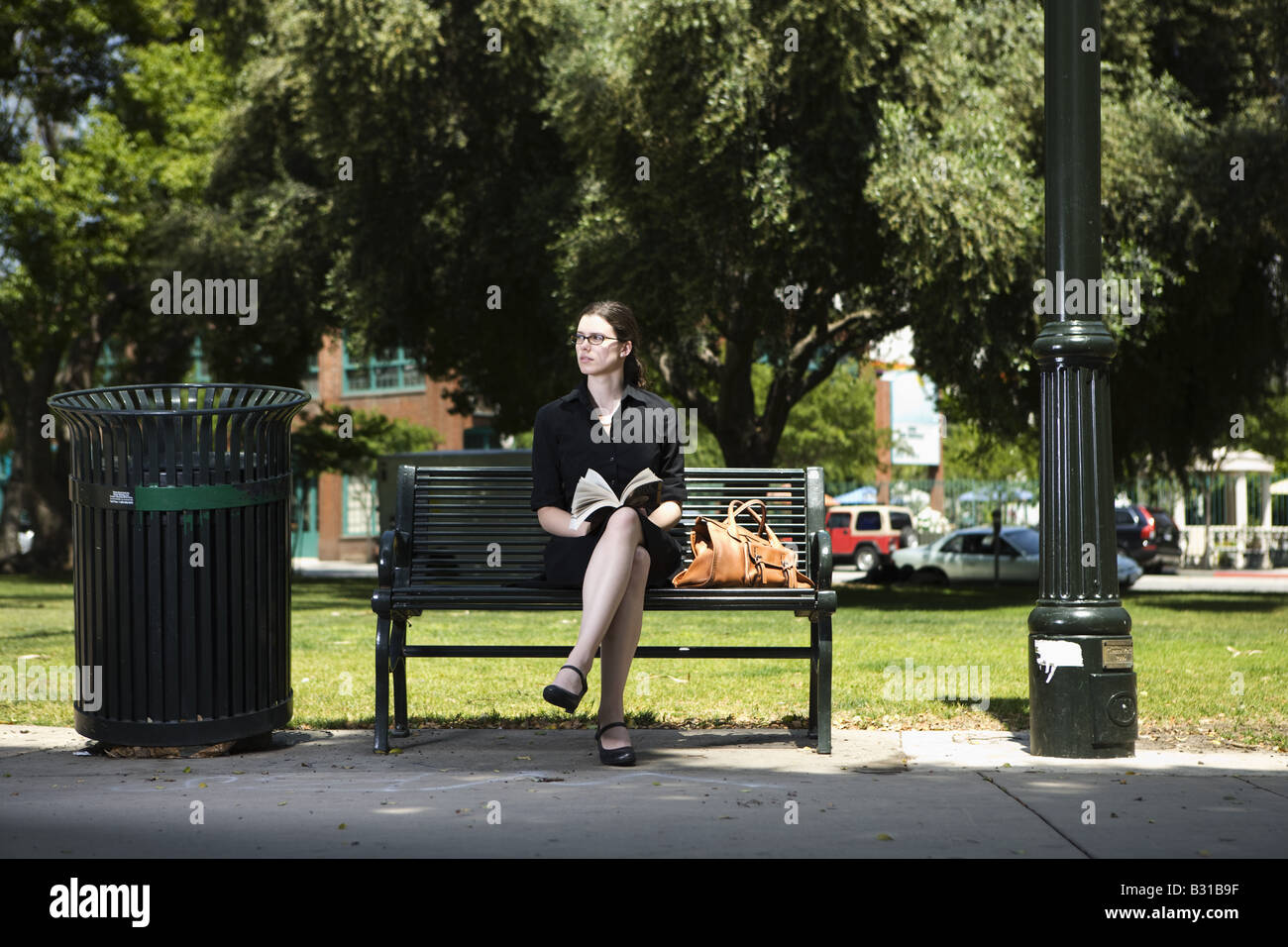 Young woman sitting on park bench with book Stock Photo
