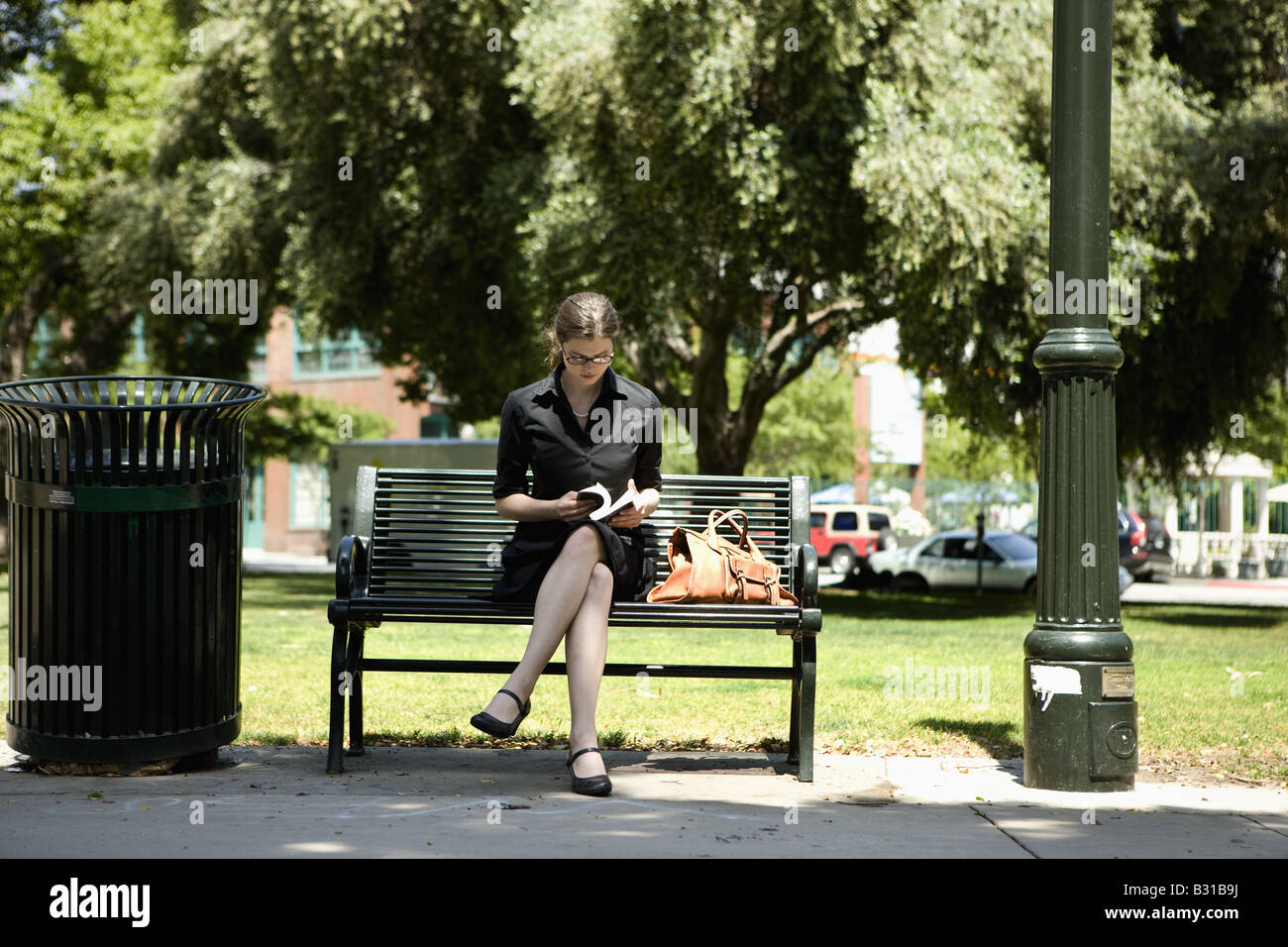 Young woman sitting on park bench reading book Stock Photo