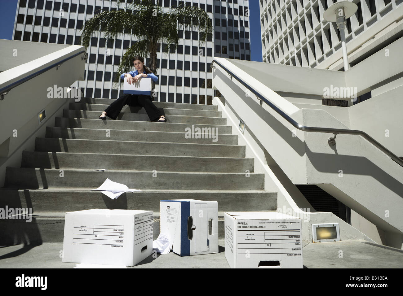 Girl Friday sitting on steps by dropped boxes of paperwork Stock Photo