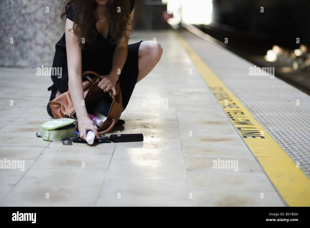 Young woman picking up spilled personal items from the floor Stock