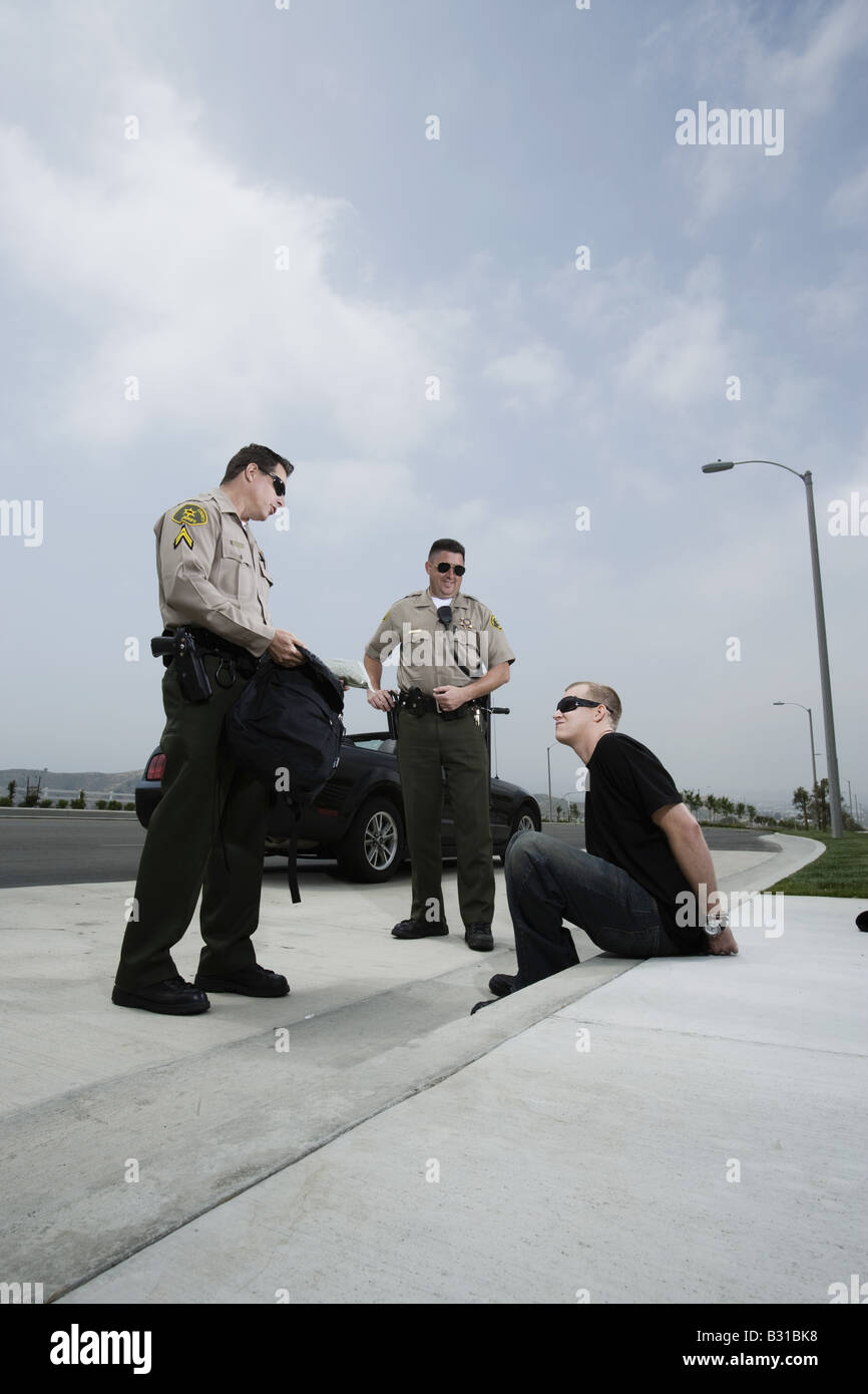Two police officers discovering drugs in backpack of arrested man Stock Photo