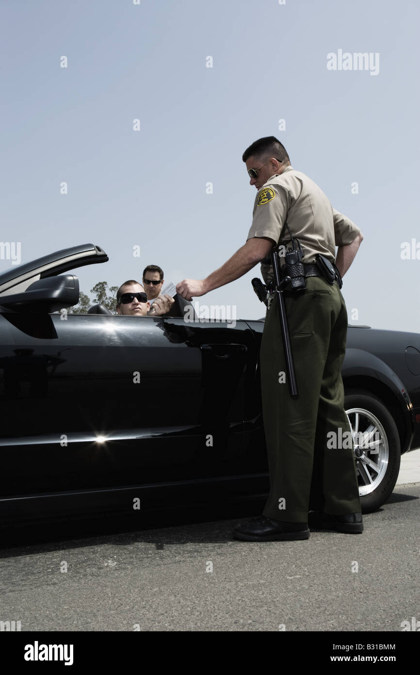 Police officer handing drivers license to man in Mustang Stock Photo