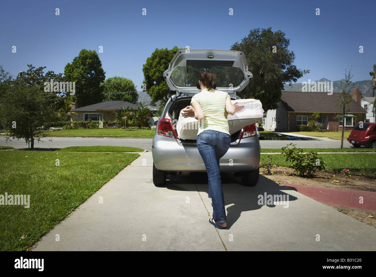 College bound girl trying to fit mattress into back of car Stock Photo
