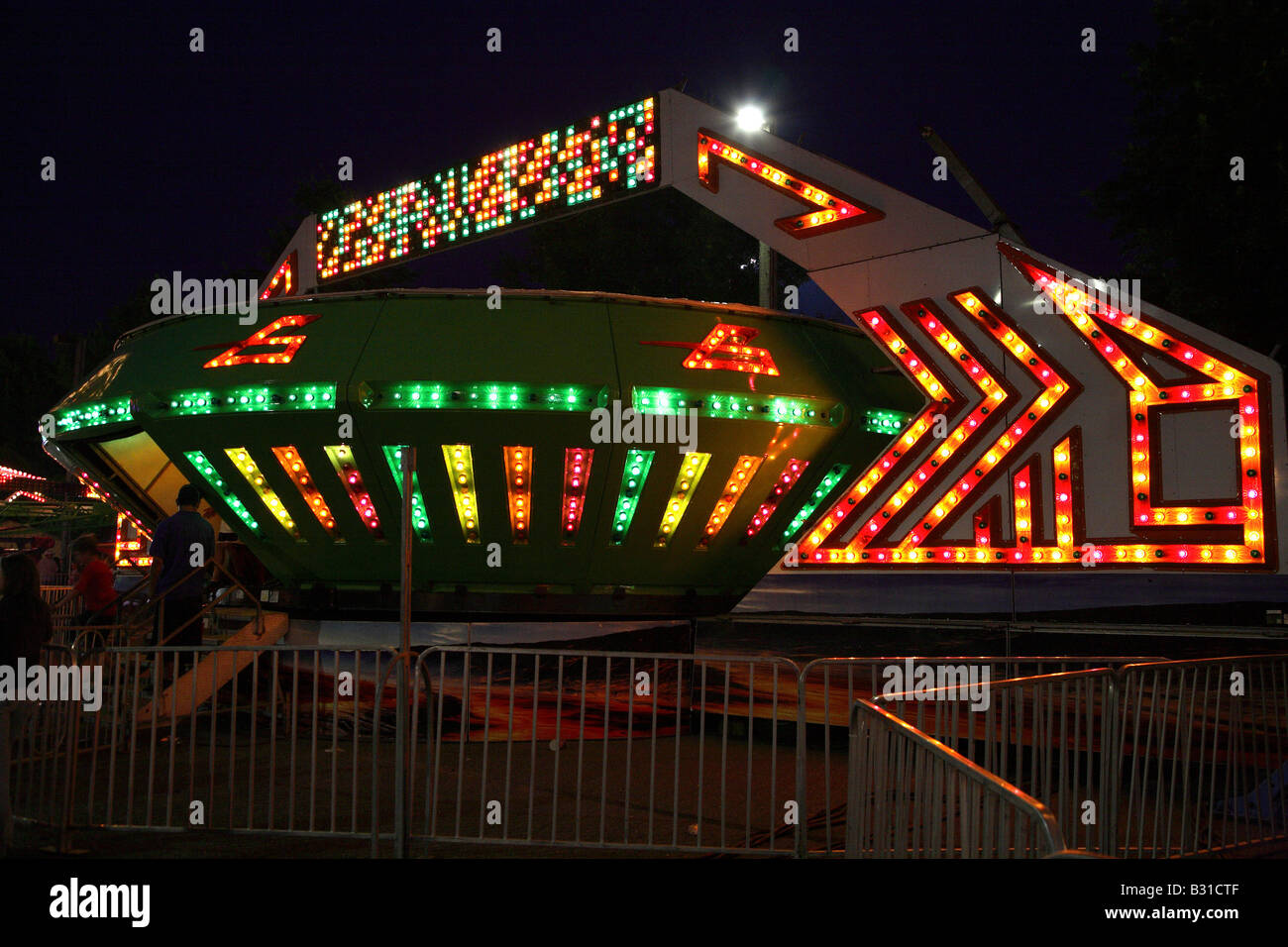 Space ship funfair ride.  Large flying saucer shape with bands of multi colored lights on the outside of fancy geometric shape. Stock Photo