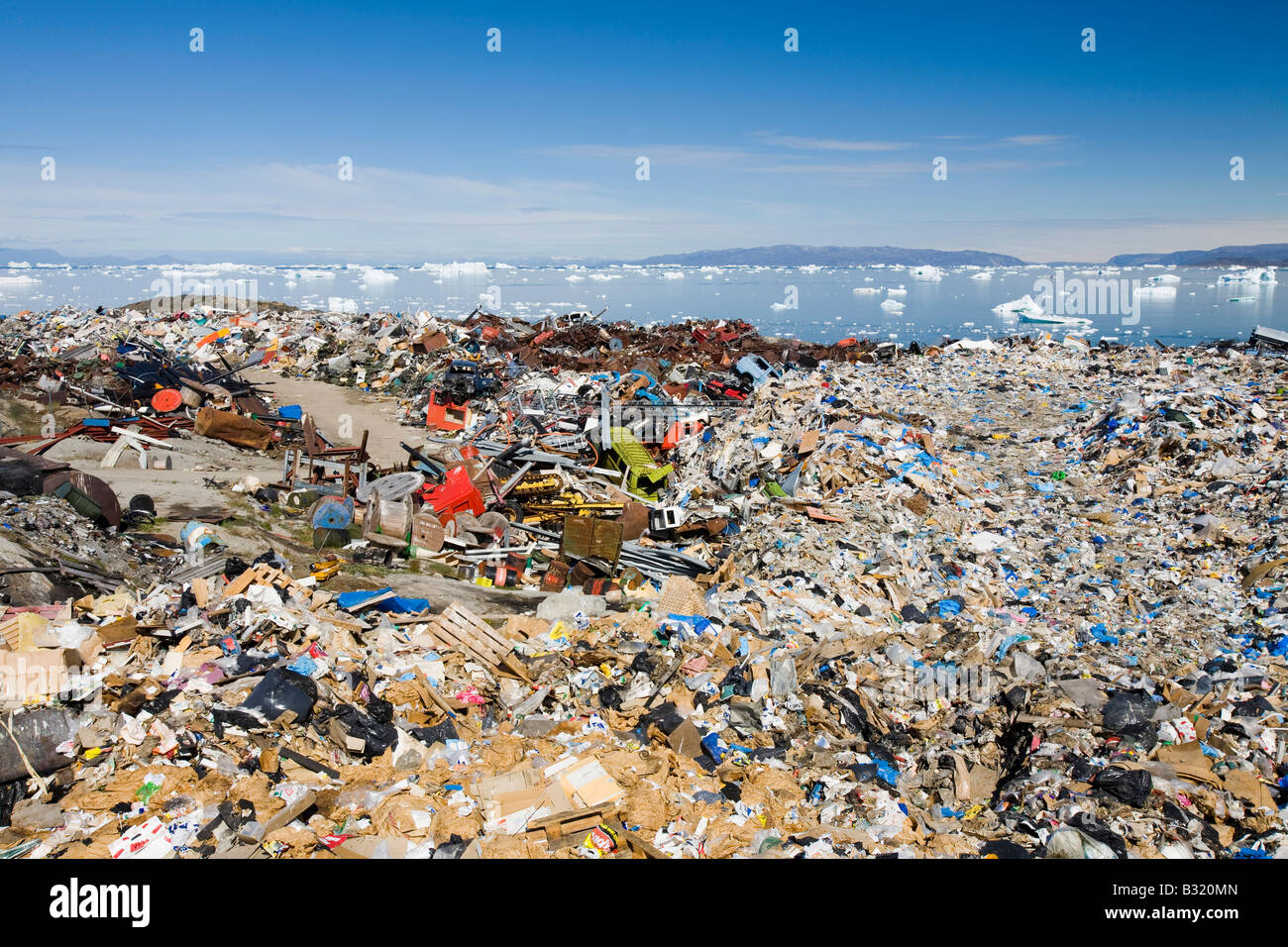 Ilulissat town rubbish dump with icebergs behind, Greenland Stock Photo