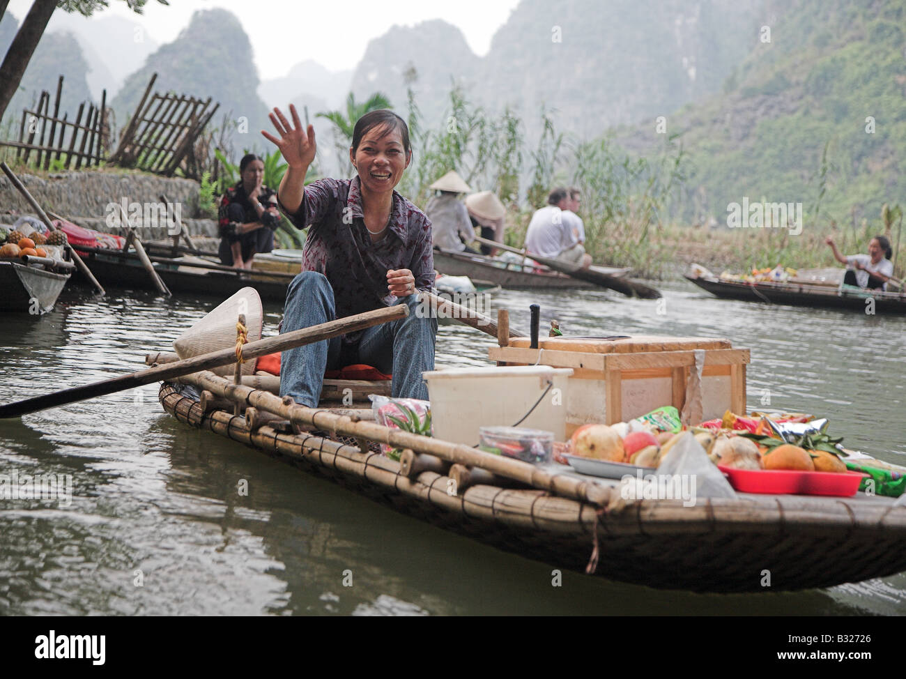 A local woman in rowboat selling snacks and softdrinks to tourists on the Ngo Dong River in Tam Coc, northern Vietnam. Stock Photo