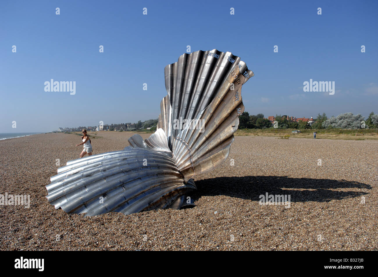 Female tourist walks by the Scallop sculpture by Maggi Hambling to celebrate the life of Benjamin Britten on Aldeburgh beach Stock Photo