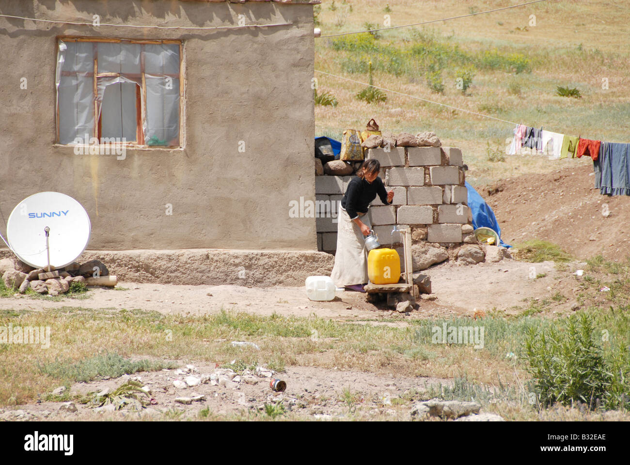 A Kurdish woman filling a container with water from a tap outside her house Stock Photo