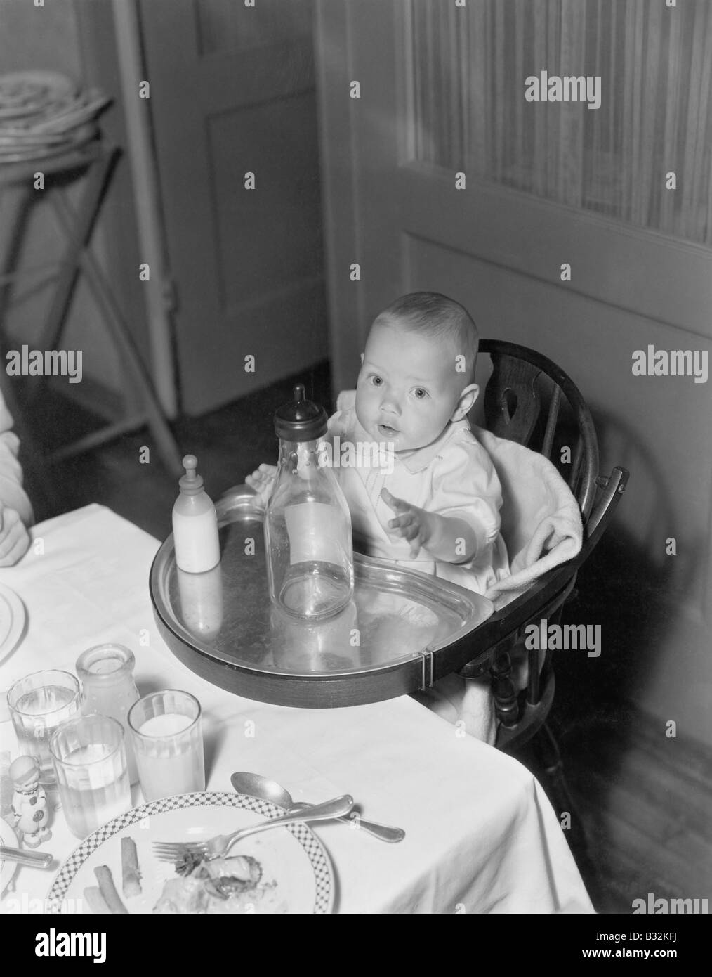 Baby in highchair with large and small bottles Stock Photo