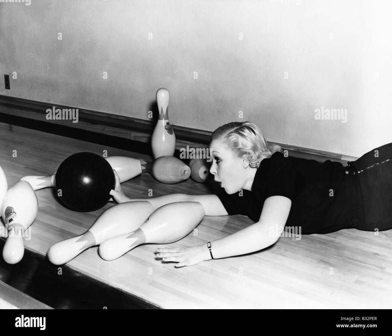Woman sliding down bowling alley with ball Stock Photo