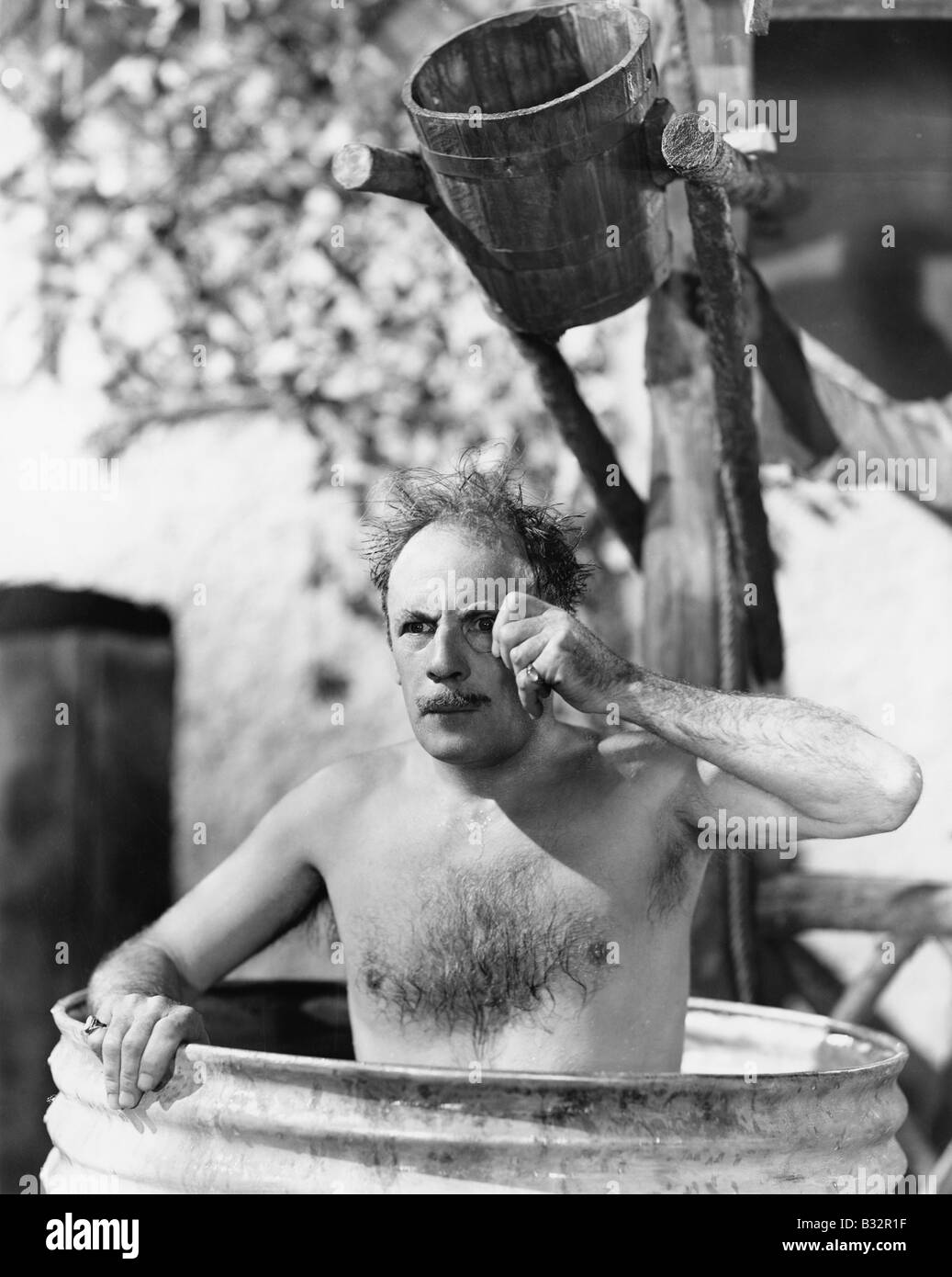 Man sitting in barrel taking bath looking through his monocle Stock Photo