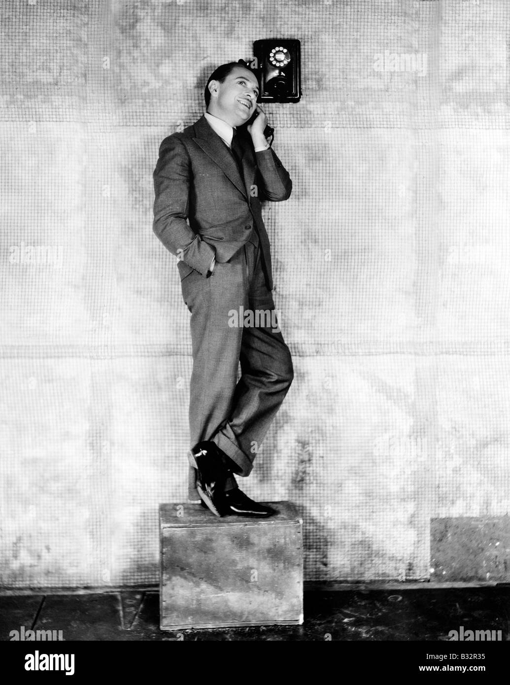 Man standing on a box to reach the telephone Stock Photo