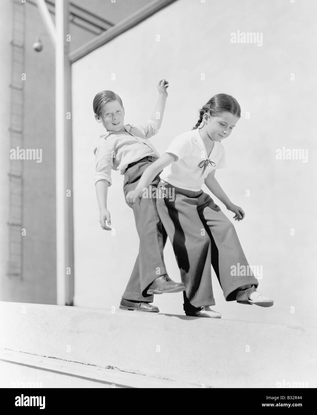 Boy and girl trying to balance on a ledge Stock Photo