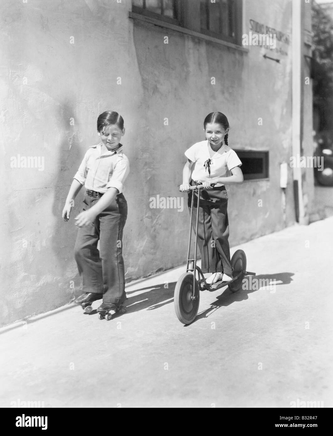 Boy and girl playing on a scooter and the other on roller blades Stock Photo