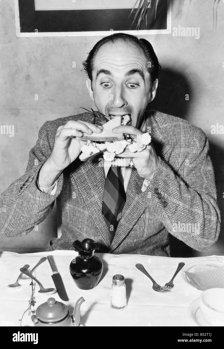 Man sitting at a dining table and trying to eat a sandwich Stock Photo