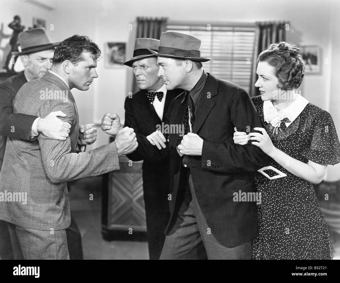 Two men fighting with each other and being held back by a woman and a man Stock Photo
