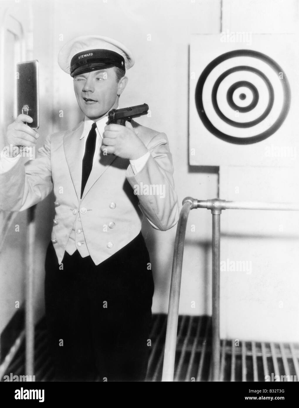 Young man looking mirror aiming dartboard with handgun Stock Photo