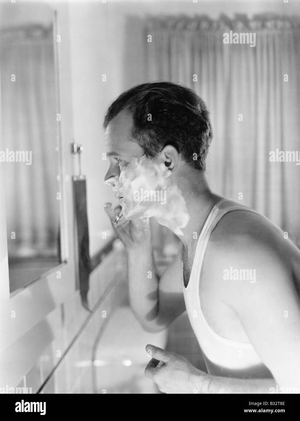 Profile of a young man in front of a mirror in a bathroom shaving Stock