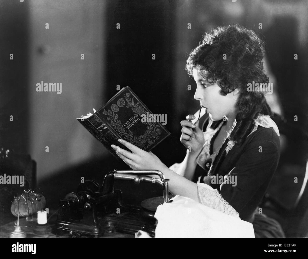 Profile of a young woman sitting and reading a book and eating Stock ...