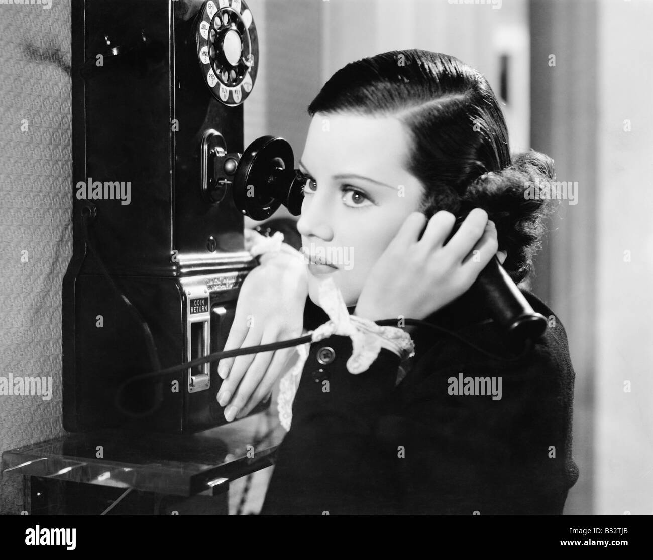 Profile of a young woman talking on a payphone Stock Photo