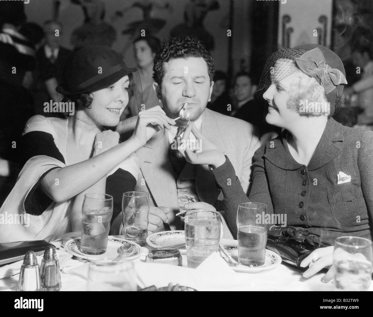 Two women lighting a cigarette for a man Stock Photo