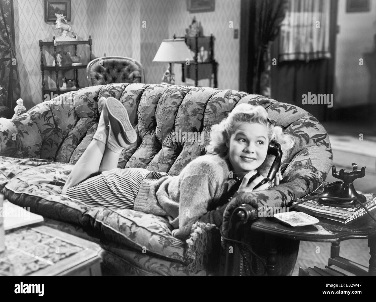 Young woman lying on a sofa in a living room and talking at the phone Stock Photo
