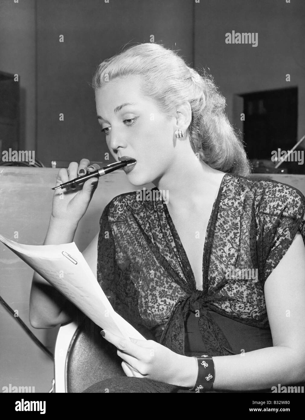 Young woman with pen in mouth, reading a letter Stock Photo