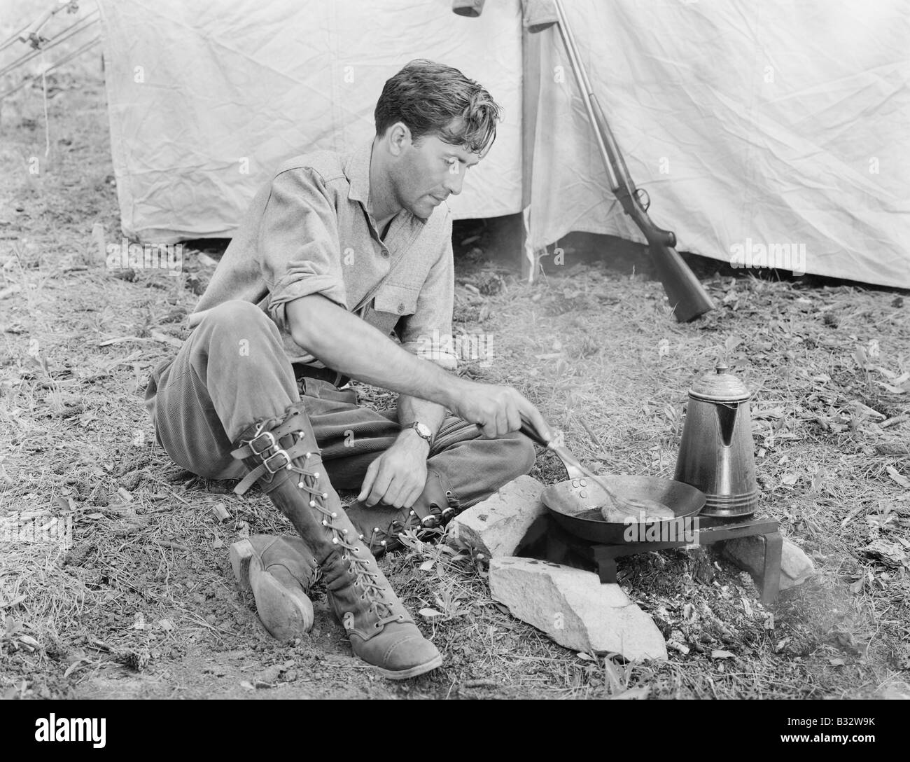 Man sitting in front of his tent preparing food Stock Photo