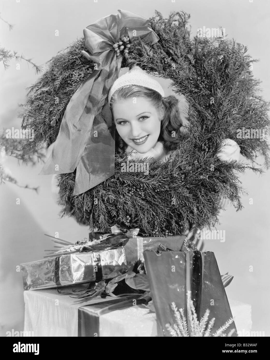 Young woman looking through wreath with presents in front her Stock Photo